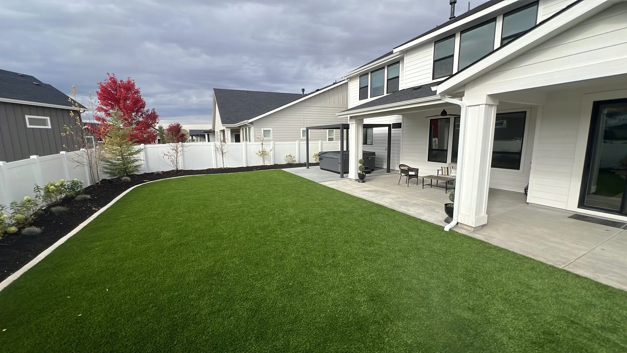 Artificial turf lawn edged with planting beds beside a covered patio and white fence
