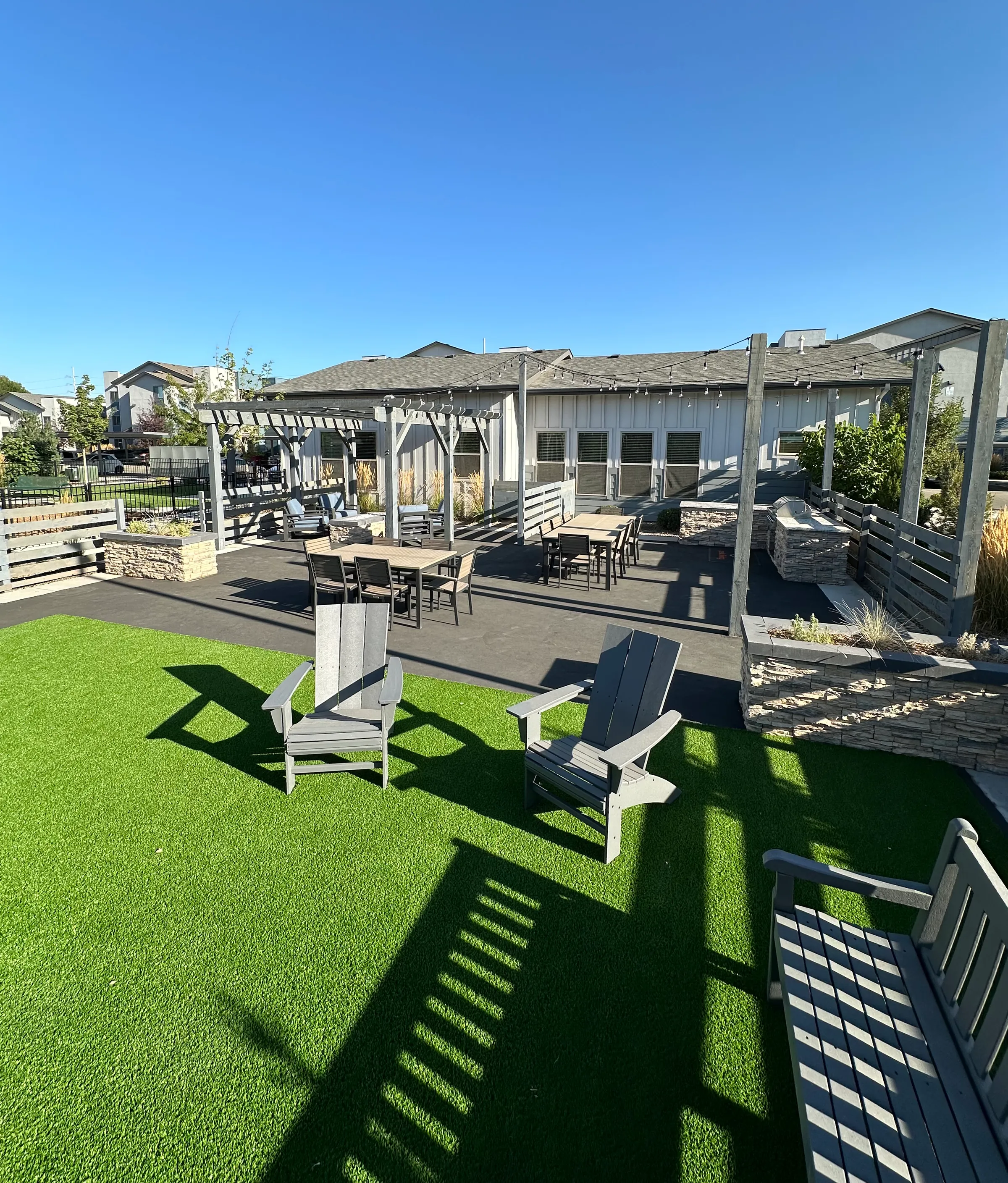 Artificial turf lounge under a gray pergola with Adirondack chairs