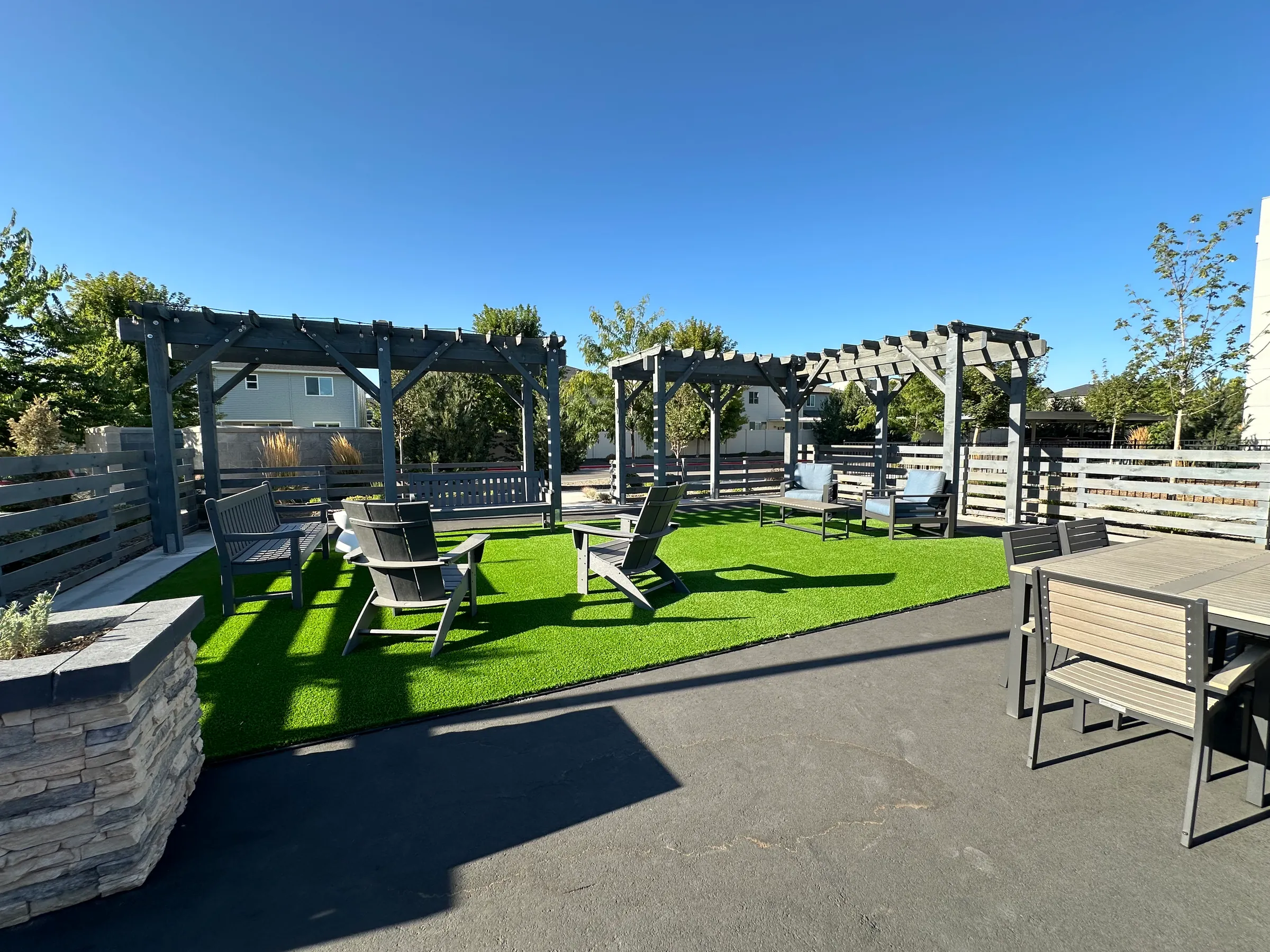Community patio with artificial turf, pergolas, seating and a stone planter