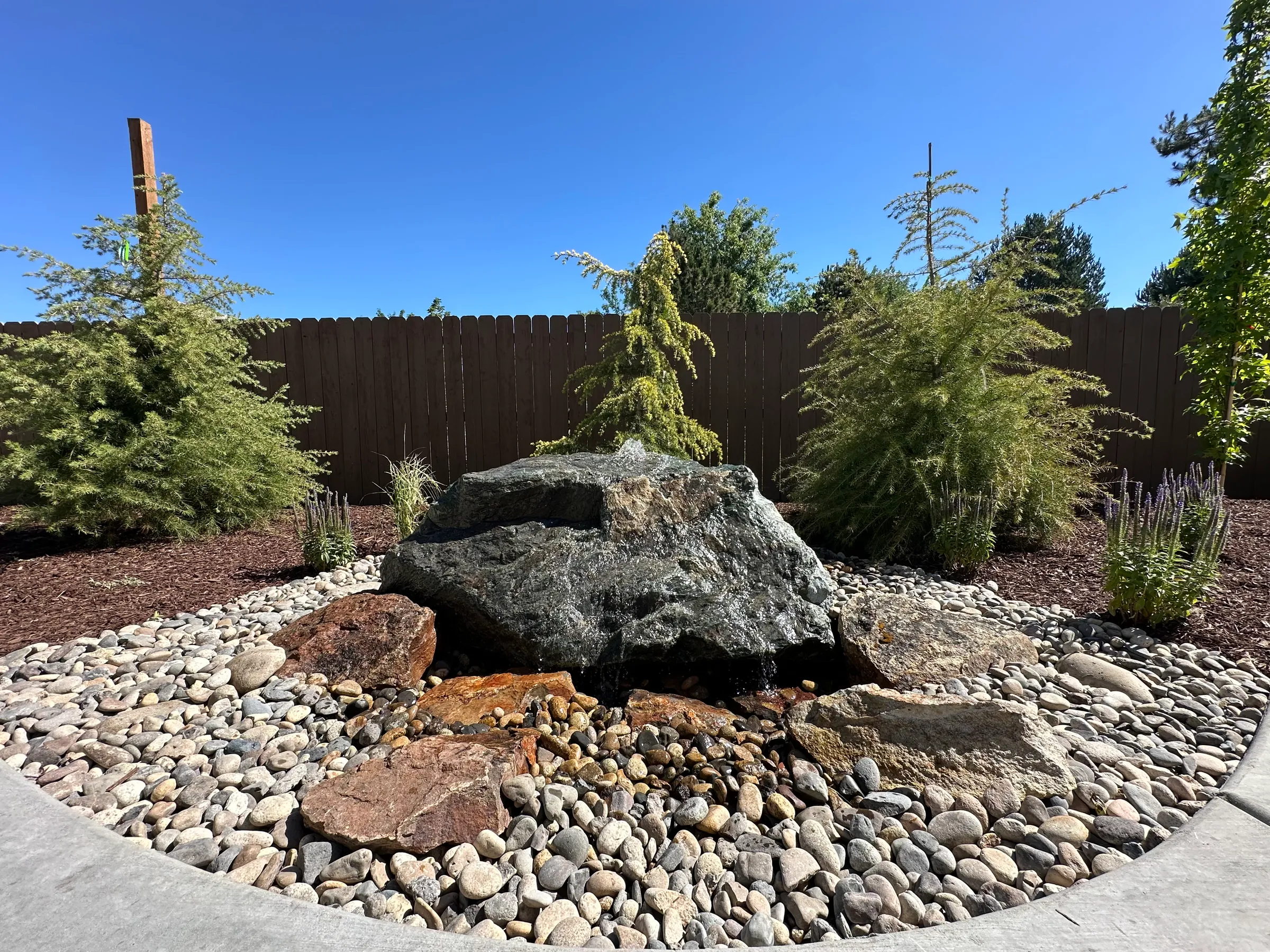 Bubbling boulder fountain set in river rock and planting beds