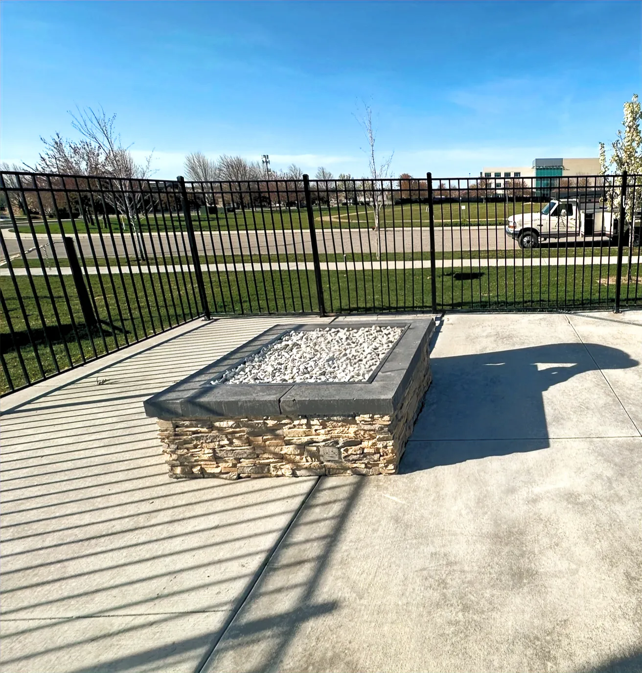 Commercial gas fire feature with a stone base on a concrete plaza behind a metal fence