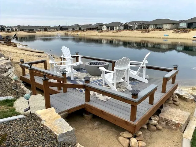 Composite deck with cedar-toned rails overlooking a lake, with Adirondack chairs around a fire bowl