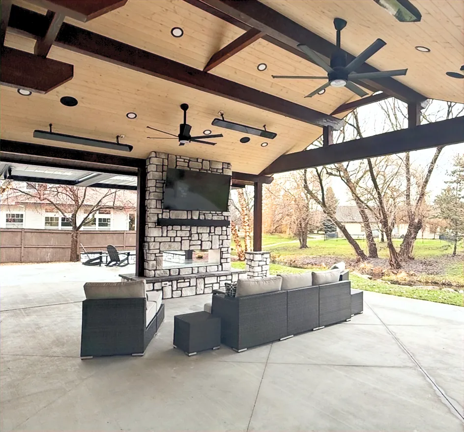 Covered patio with a stone fireplace, mounted TV, ceiling fans and overhead heaters