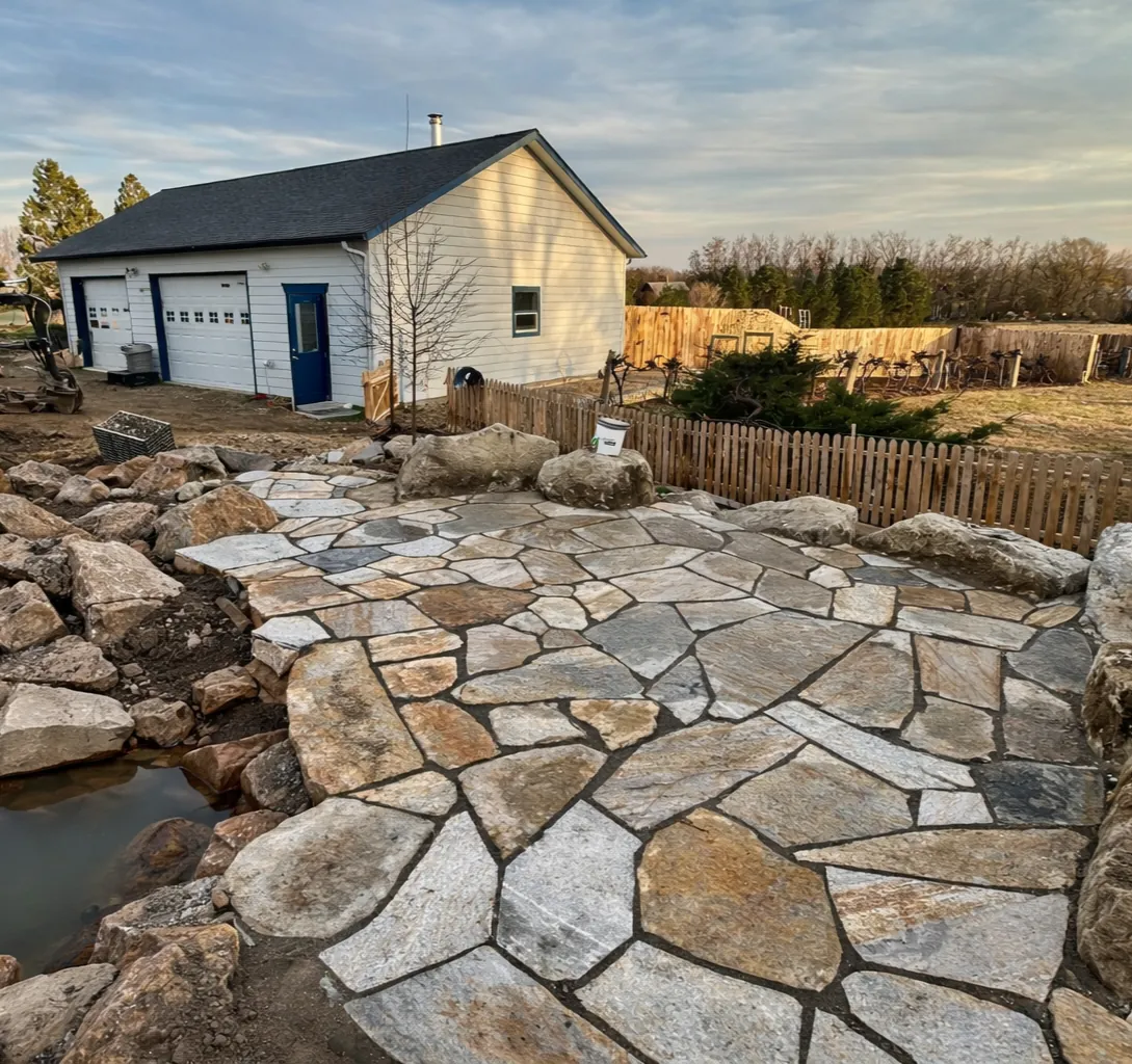 Custom-cut flagstone patio wrapped around a stone water feature with boulders