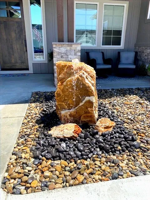 Drilled rock fountain in a river-rock bed beside a front entry