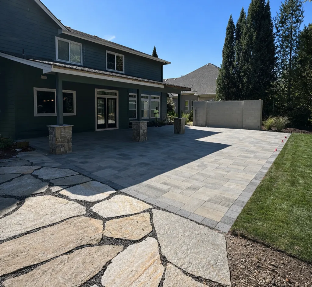 Large-format paver patio flowing into natural flagstone set in dark gravel beside stone-wrapped columns