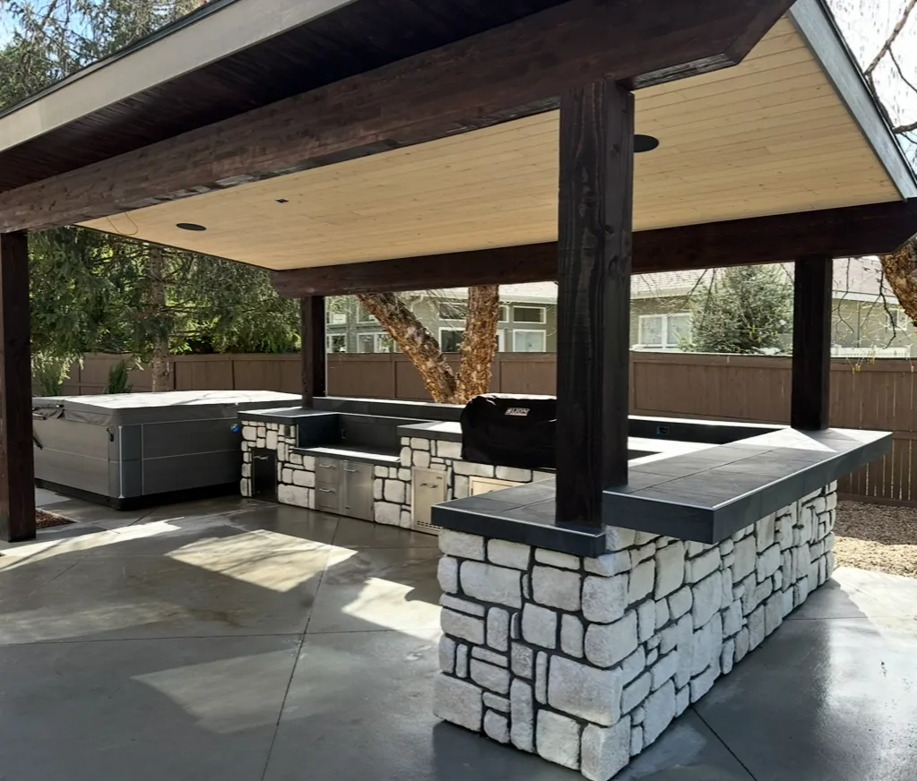 Timber structure sheltering a stone outdoor kitchen island and a spa