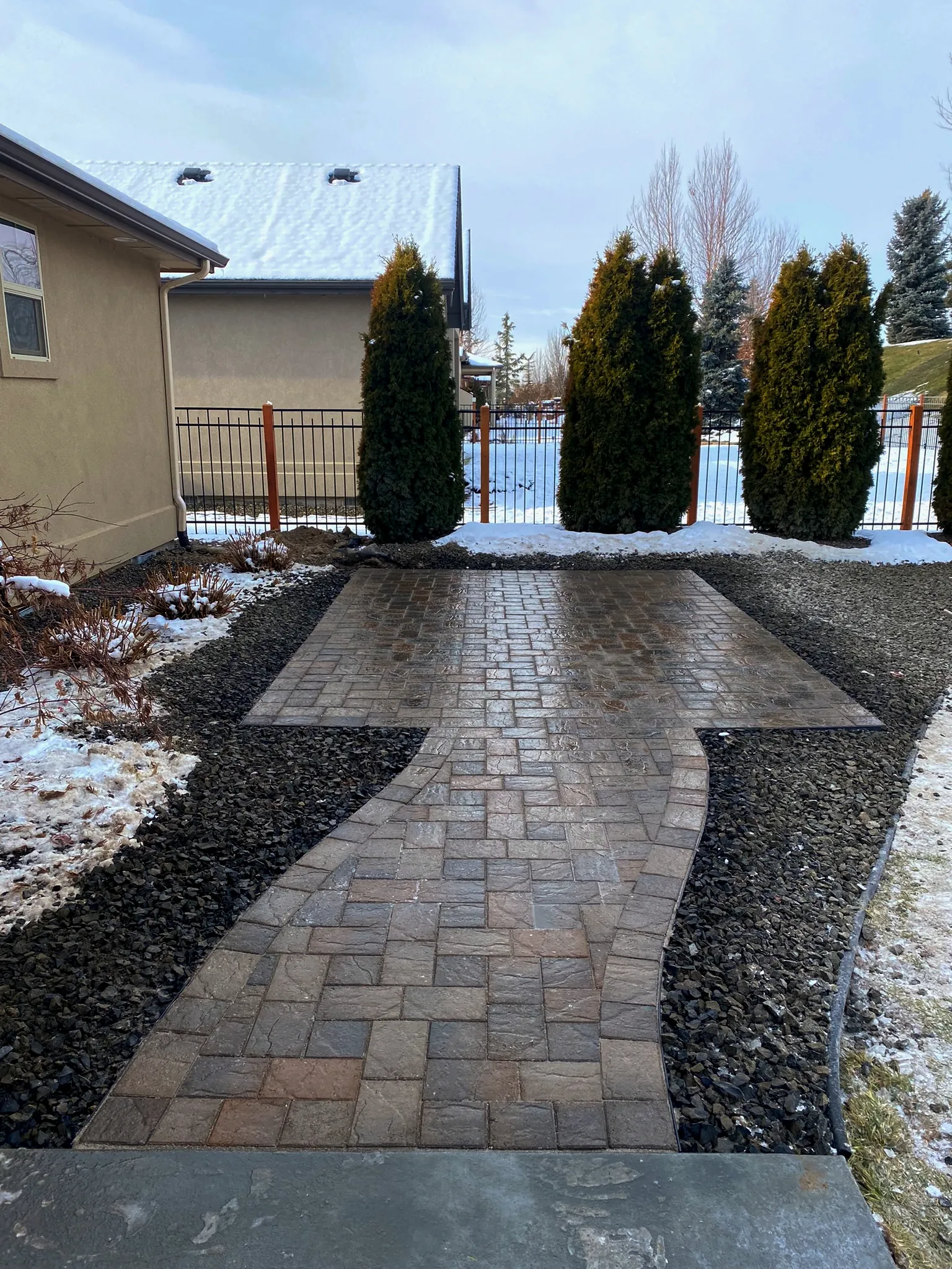 Paver walkway with a soldier border leading through dark rock beds to a backyard patio