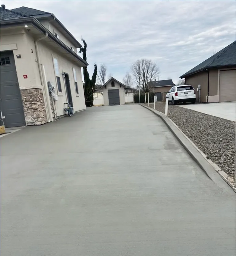 Side-yard concrete parking pad graded to drain along a garage
